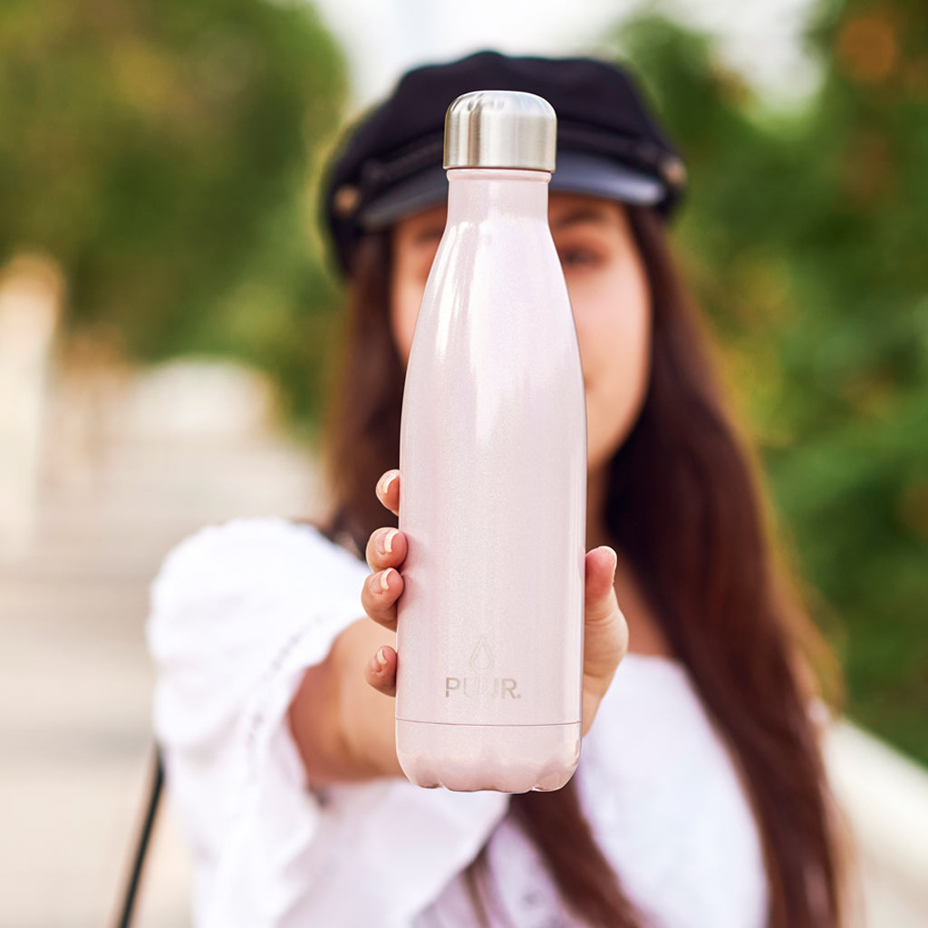 BOTELLA DE ACERO INOXIDABLE 500 ML ROSADO TORNASOL UNICORNIO, MARCA PUUR EN MANOS DE MUJER